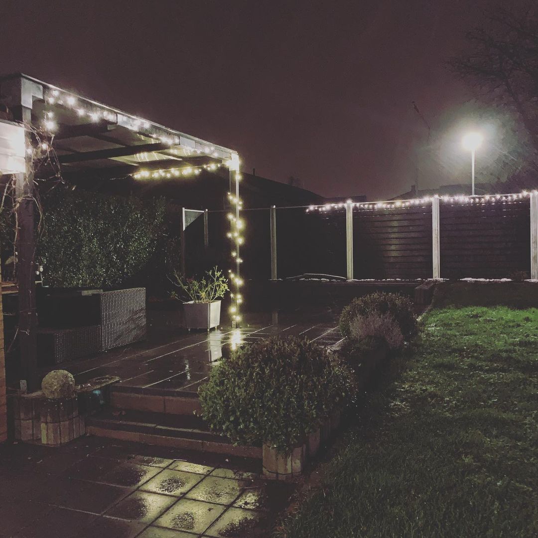 En hyggelig vinterhave med julelys på komposithegn og pergola